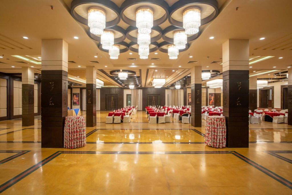 Prostrana sala za banket sa visećim lusterima i redovima stolova sa crvenim stolnjacima.